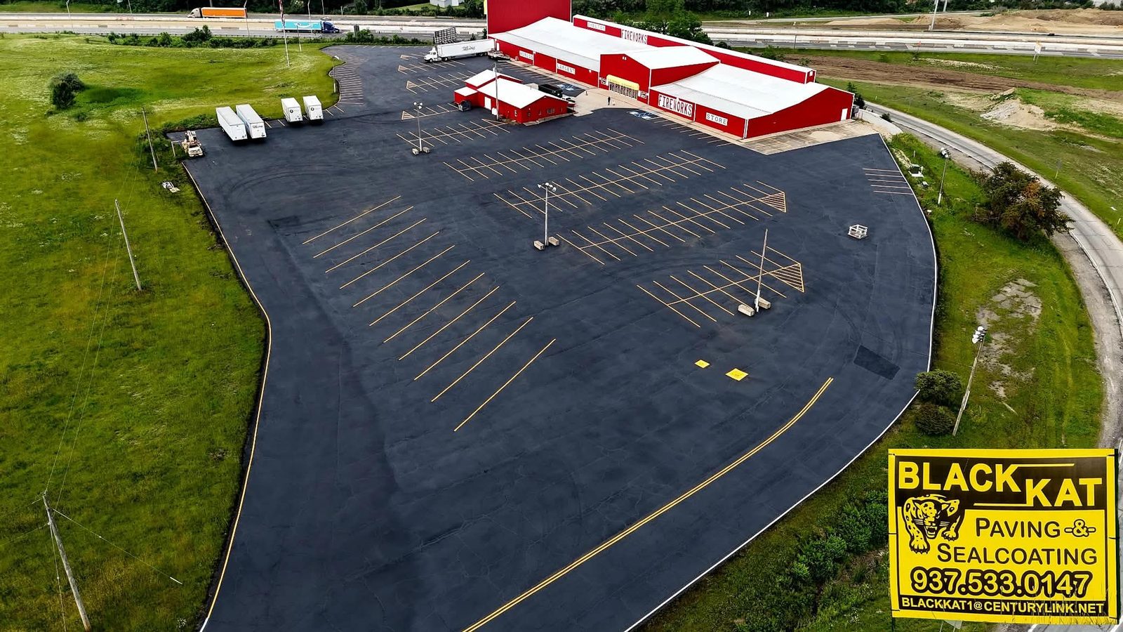 Drone view of a freshly sealcoated commercial lot with crisp parking-stall striping by Blackkat Paving